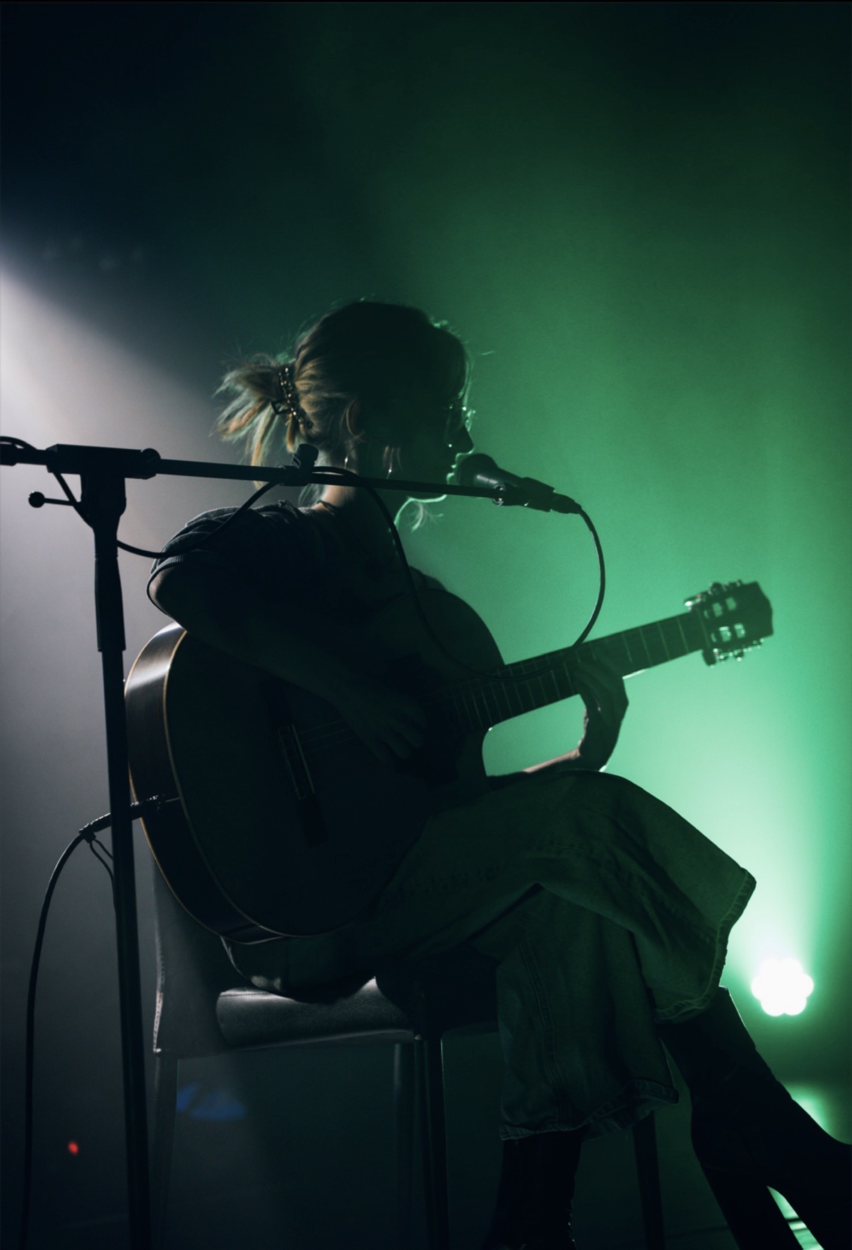 Een muzikant zingt en speelt gitaar in groen podiumlicht